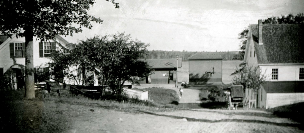 In a scene that shows the first railroad station at Lakeside with Lake Messalonskee in the background, we see the Richardson/Williams home on the left and the Judkins/Butterfield house on the right (no longer standing). A note informs that the Judkins home had a dance hall on the second floor, where during the “old cider times” things on occasion got rough. Frank and Ella Richardson Judkins lived on the first floor under the dance hall, and Nina and Joe Butterfield had a store on the westerly side of the building.